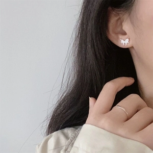 Close-up of small silver butterfly earrings with lava texture and zircon on earlobe