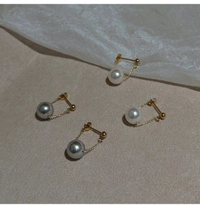 Detail of round pearl drop earrings with gold chains on elegant beige fabric backdrop