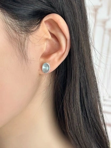 Close-up detail of silver oval aquamarine stud earring worn on a female model ear