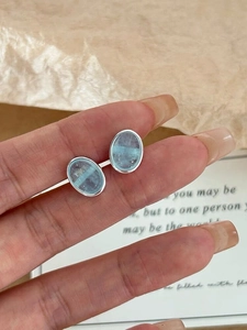 Close-up of elegant S925 silver oval aquamarine earrings held against a poetic backdrop