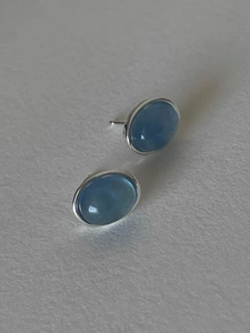 Detailed macro view of S925 silver oval aquamarine studs on white textured background