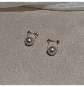 Elegant U-shaped gold chain earrings featuring round grey pearls on textured beige background