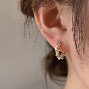 Detailed view of twisted gold-plated hoop earrings with delicate pearls on ear