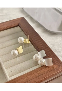 Détail de boucles d'oreilles carrées en métal brossé avec perles dans un écrin à bijoux