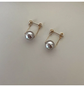 Detail of grey pearl earrings with gold chain pendant on a textured cream surface