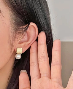 Détail d'une boucle d'oreille en argent S925 carrée dorée avec perle blanche sur l'oreille
