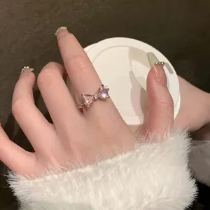 Close-up of a silver bow ring with pink zircon on finger with a white coffee cup