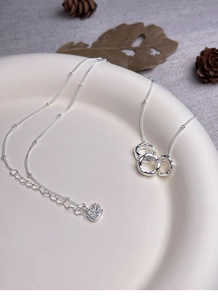 Macro detail of S925 sterling silver triple interlocking ring necklace on ceramic tray