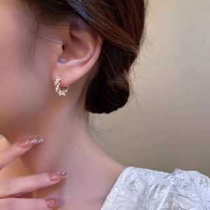 Detailed close-up of golden vine-shaped C-hoop earrings with white pearls on a model