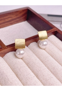 Détail de boucles d'oreilles carrées en métal brossé doré avec perles blanches pendantes