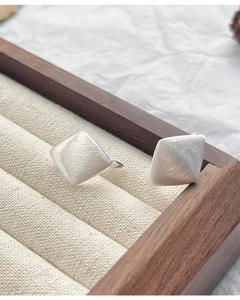 Detail view of rhombic silver earrings with a brushed matte finish on a linen display