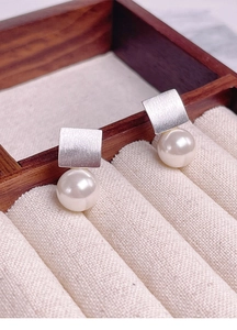 Détail de boucles d'oreilles carrées en argent brossé avec perles blanches sur velours