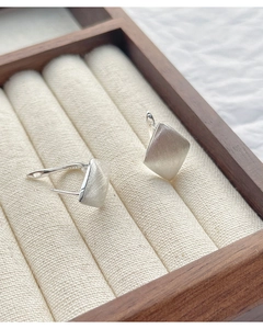Macro view of geometric rhombus silver earrings with brushed texture on wooden display case