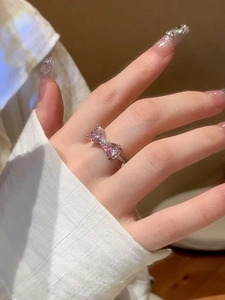 Close-up of pink bow ring with silver band worn by a model in soft indoor lighting