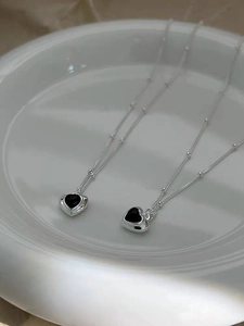 Detail view of two S925 sterling silver heart-shaped black agate necklaces on a white tray