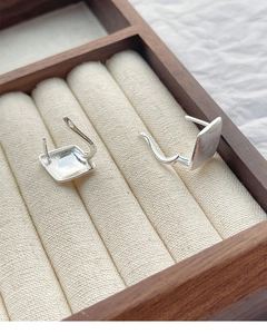 Macro shot of silver geometric square earrings with brushed metal finish on wood display