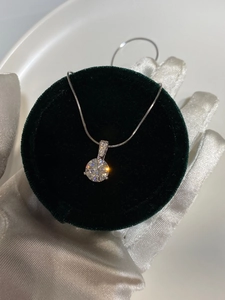 Macro shot of a classic round-cut diamond pendant on a silver chain over green velvet