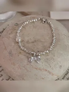 Detail of silver beaded bracelet featuring irregular beads, a white pearl, and a bow charm