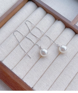 Macro detail of long silver pearl threader earrings displayed in a luxury white jewelry box