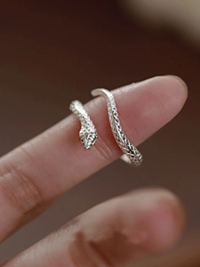 Detail of silver snake ring with green gemstone eyes and textured scales on finger