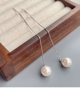 Detail view of long S925 sterling silver drop earrings with elegant white pearls on a tray