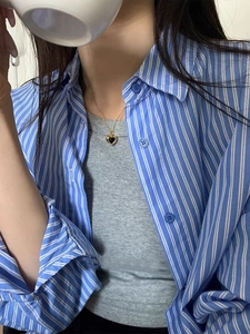 Detail of a gold necklace with heart-shaped black onyx pendant worn on a striped shirt