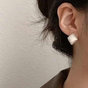 Macro shot of silver geometric square earrings with brushed texture on model ear