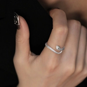 Detail of silver snake ring with green stone eyes and scale texture on model finger