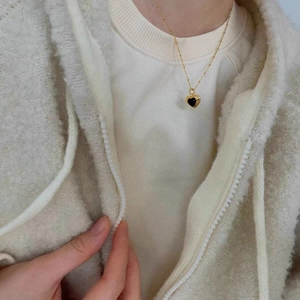 Detailed close-up of a gold heart pendant with black onyx on a delicate beaded chain
