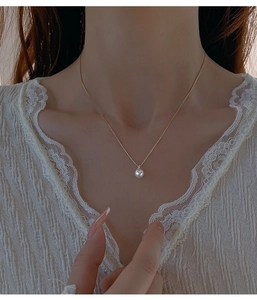 Primo piano di un elegante ciondolo di perla su catena d'oro sottile con pizzo bianco