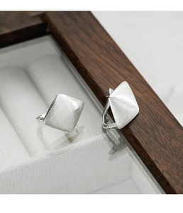 Macro detail of silver geometric rhombus earrings with brushed metal texture and matte finish
