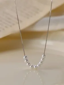 Vue macro d'un collier en argent S925 minimaliste avec sept perles blanches sur un bureau