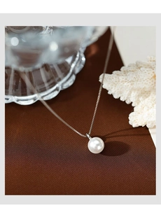 Dettaglio di una perla bianca tonda su una sottile catena in argento su tessuti di lusso