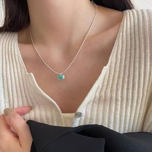 Detail of S925 silver necklace with a rectangular green stone on beige knit sweater