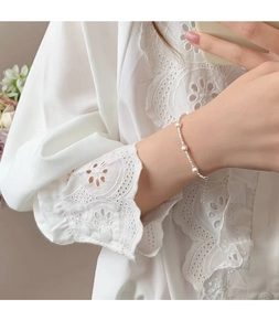Detail von S925 Silberperlenarmband mit Perlen am Handgelenk vor weißem Spitzenhintergrund
