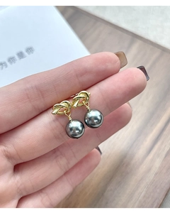Detailed view of gold knot pearl earrings with dark grey pearls held by a hand