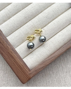 Detailed view of gold knot earrings with dark grey pearls in a luxury wooden jewelry box