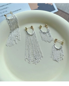 Détail de boucles d'oreilles à pompons argentés et accents dorés sur assiette