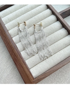 Détail de boucles d'oreilles à pompons argentés avec accents dorés sur plateau