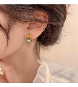Detailed view of elegant gold knot earrings with hanging grey pearls on a female model