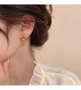 Detail of elegant gold knot earring featuring a lustrous grey drop pearl on female model