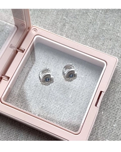 Détail de boucles d'oreilles cœur en argent avec gemme bleue dans une boîte rose