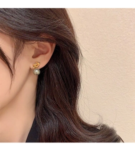 Detailed view of an elegant gold knot earring with a dark grey pearl on a female model