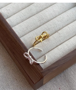 Macro shot of silver and gold bow rings displayed on a textured jewelry tray