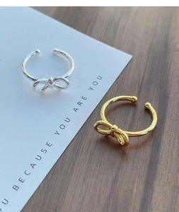 Detailed view of silver and gold bow-shaped open rings on a minimalist card background