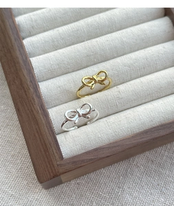 Close-up of gold and silver bow rings on a minimalist display stand with linen texture