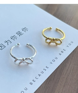 Detail of bow-shaped adjustable rings in silver and gold on a minimalist card