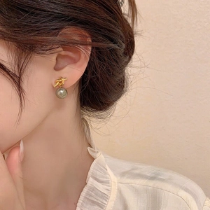 Elegant gold knot stud earrings with metallic grey pearl drop shown on a model