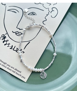 Macro shot of S925 silver pearl bracelet with Fu character pendant on ceramic tray