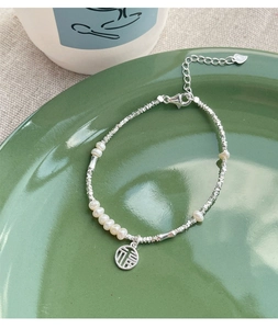 Detail of S925 silver pearl bracelet featuring a Fu charm on green ceramic plate